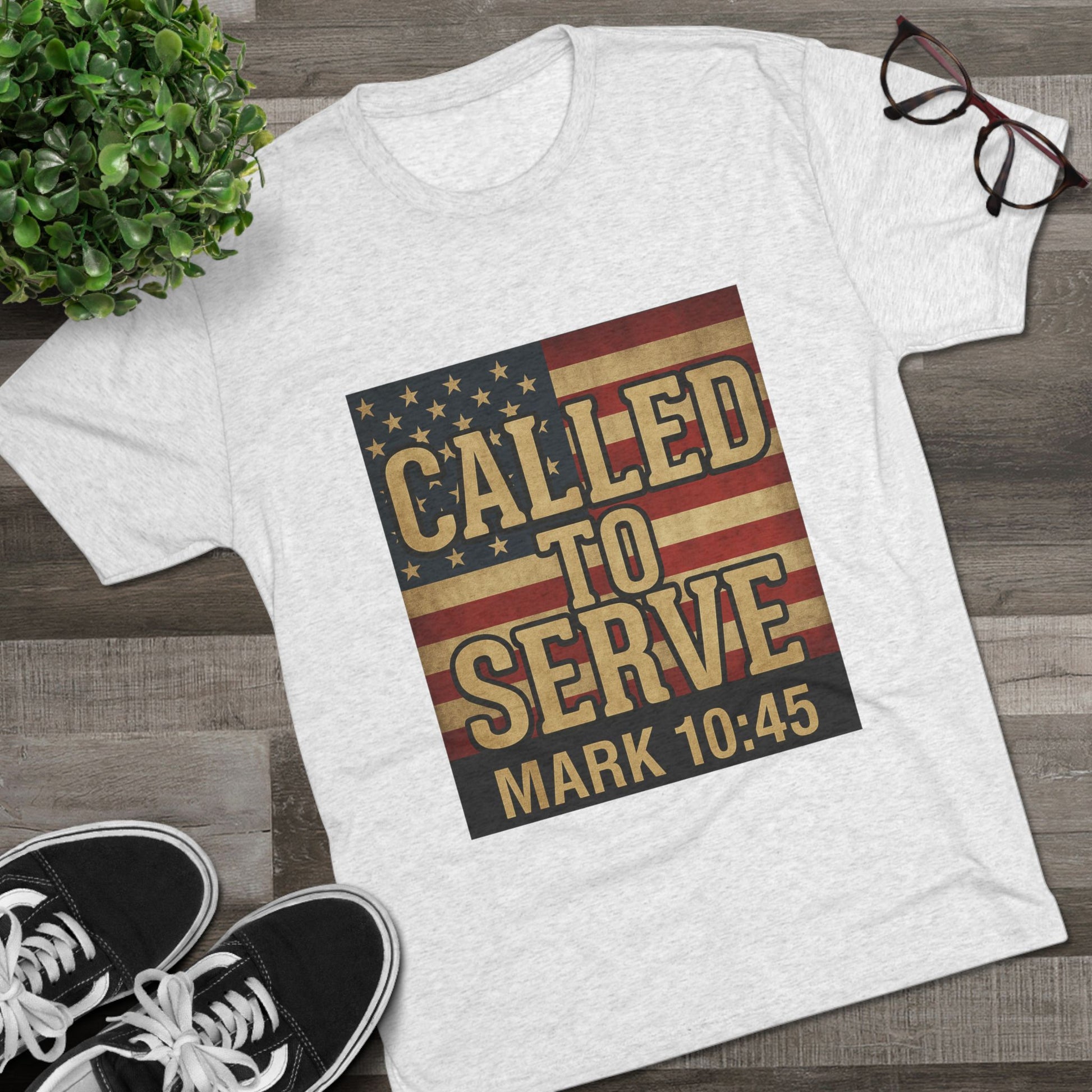 White t-shirt with American flag design and 'Called to Serve' text on a wooden surface with shoes and glasses.